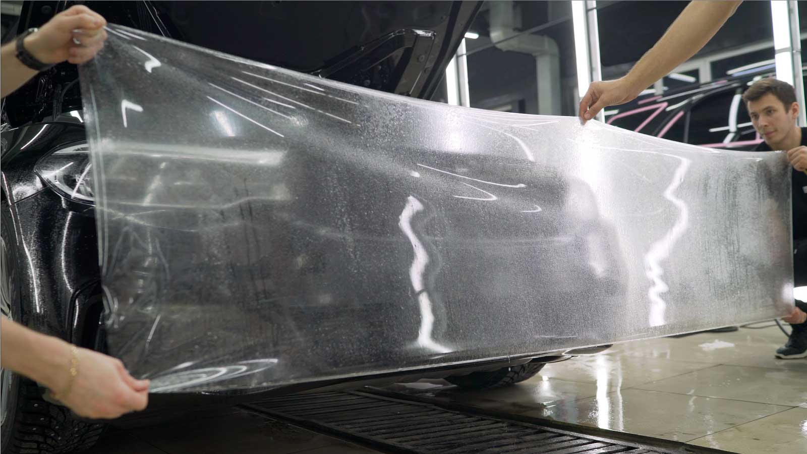 two installers holding paint protection film before applying it to the bumper of a vehicle