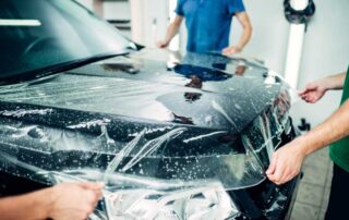 two installers applying paint protection film to the hood of a vehicle